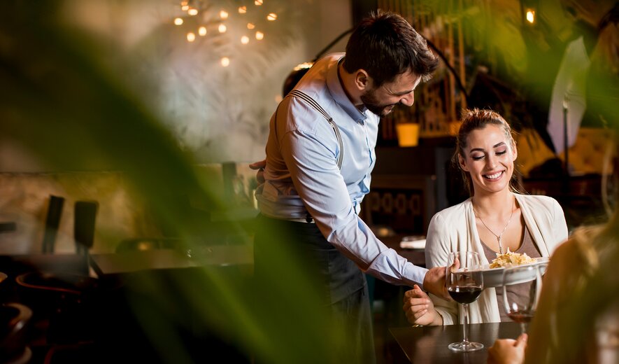 Kellner serviert lächelnder Frau ein Gericht in einem stilvollen Restaurant – freundlicher Service und angenehme Atmosphäre